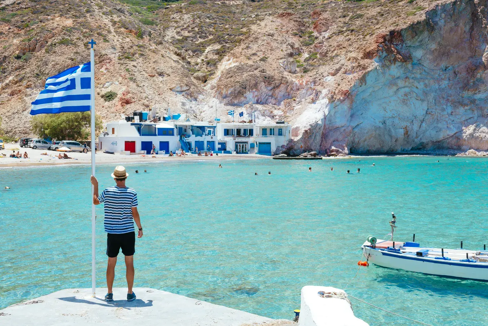 Man stands on dock with greek flag on coast